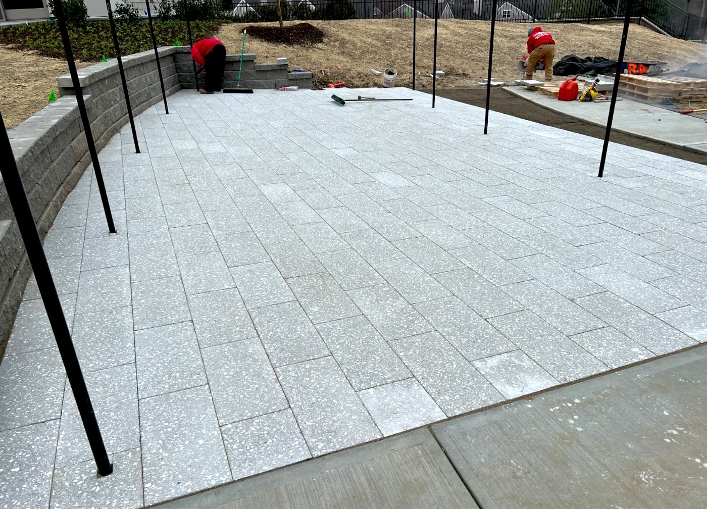Light grey paver patio with pergola posts set and a block seat wall